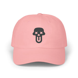 A pink graphic baseball cap featuring a black skull logo with stars for eyes and a playful tongue out design.