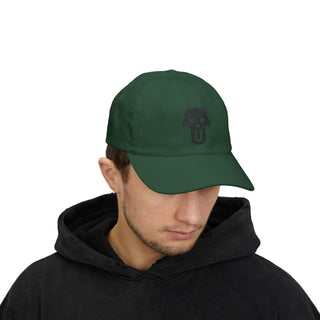 A person wearing a dark green cap with a black skull logo, paired with a black hoodie, against a plain background.