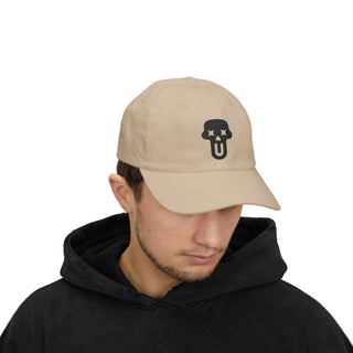 A person wearing a black graphic hoodie and a beige cap featuring a skull logo with an expressive face design.