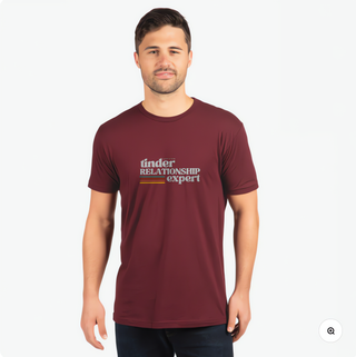 A man wears a maroon t-shirt featuring the text "tinder RELATIONSHIP expert" in a casual setting.